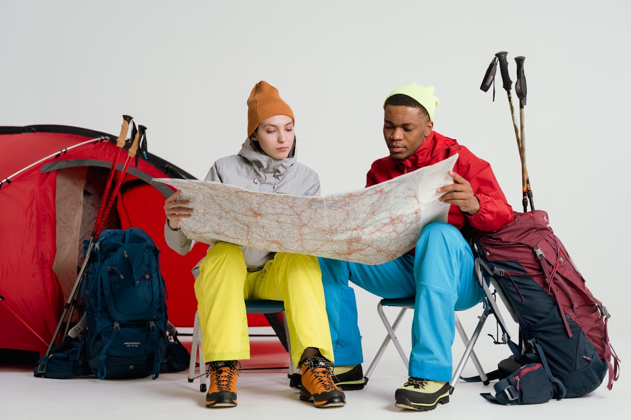 Two young hikers study a map, preparing for a winter trek with camping gear and equipment.